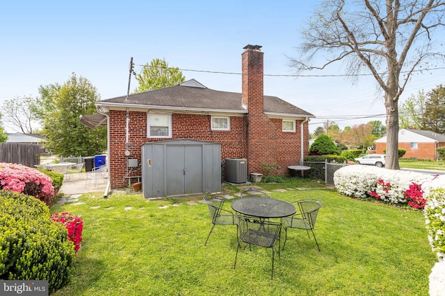 rear view of property with a chimney, fence, a storage shed, central AC, and a lawn