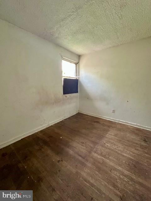 empty room featuring a textured ceiling, baseboards, and wood finished floors