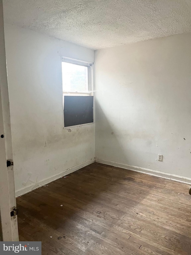 spare room featuring a textured ceiling, baseboards, and hardwood / wood-style floors