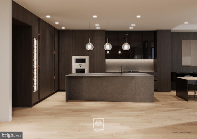 kitchen featuring a sink, a kitchen island with sink, white double oven, light wood-type flooring, and modern cabinets