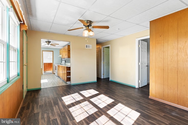 unfurnished living room with a ceiling fan, visible vents, baseboards, dark wood-style floors, and a drop ceiling