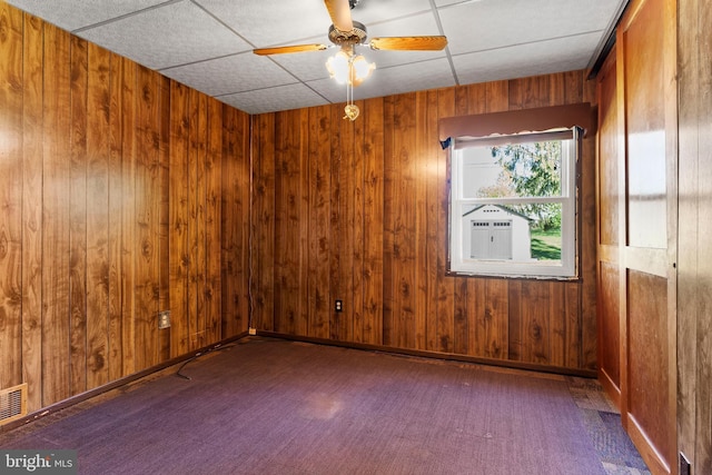 unfurnished room with wooden walls, a ceiling fan, a paneled ceiling, and visible vents