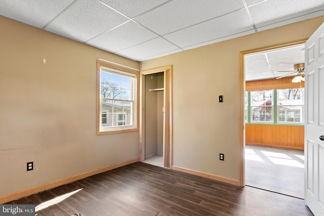 unfurnished bedroom featuring baseboards, a paneled ceiling, wood finished floors, and multiple windows