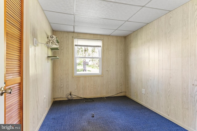 carpeted spare room featuring wood walls and a paneled ceiling