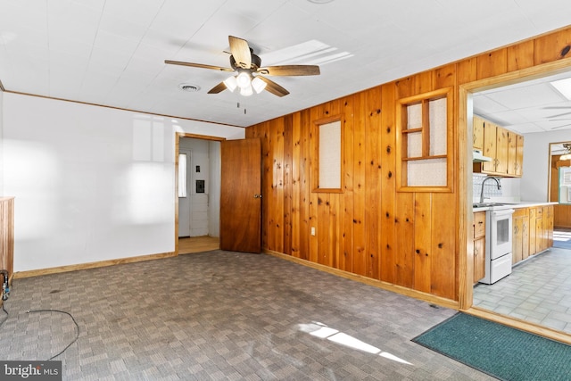 unfurnished living room featuring wooden walls, a ceiling fan, and baseboards