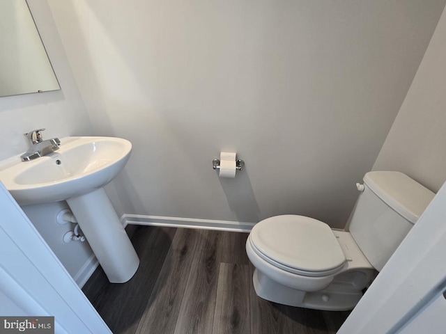 half bathroom with baseboards, wood finished floors, and toilet