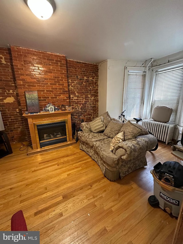 living room featuring brick wall, radiator, a glass covered fireplace, and wood finished floors