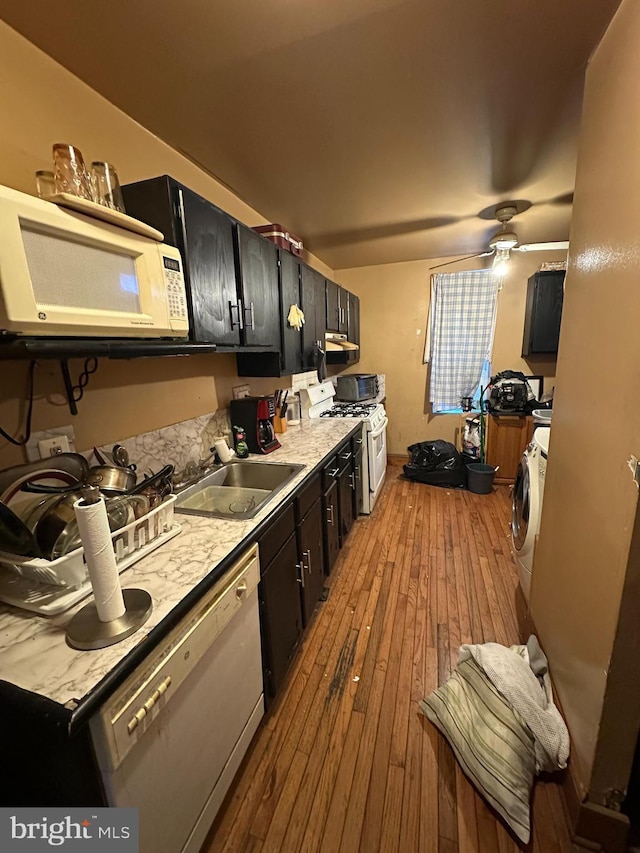 kitchen with wood-type flooring, washer / dryer, white appliances, dark cabinetry, and a sink