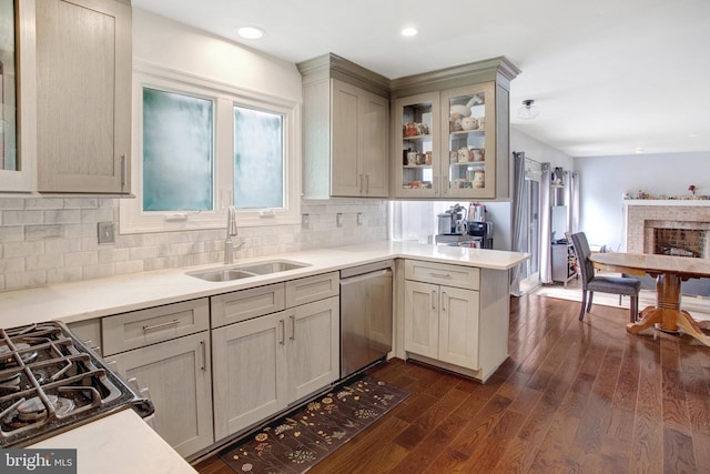 kitchen featuring a sink, dishwasher, backsplash, glass insert cabinets, and dark wood finished floors