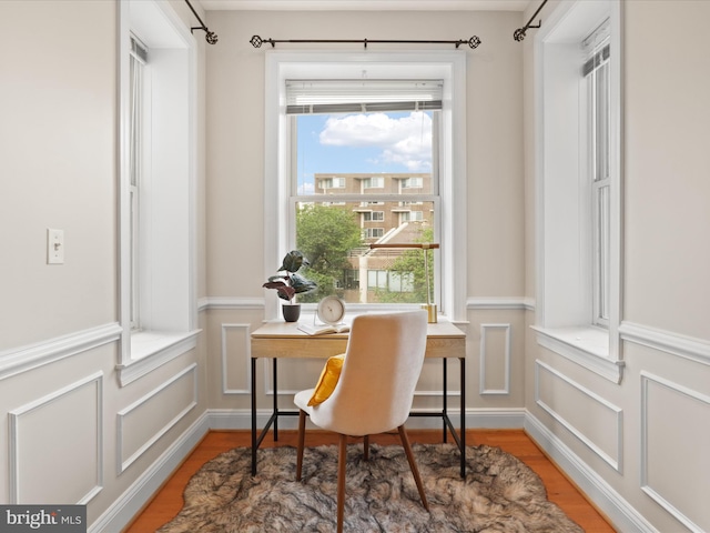 office with a decorative wall, a wainscoted wall, and light wood-style flooring