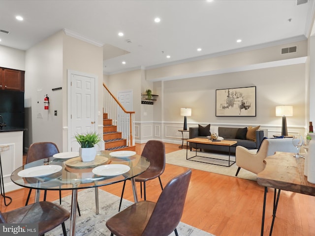 dining space with stairway, light wood finished floors, crown molding, and a decorative wall