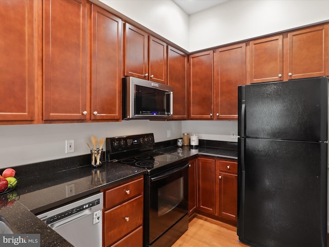 kitchen with dark stone counters, black appliances, and light wood-type flooring