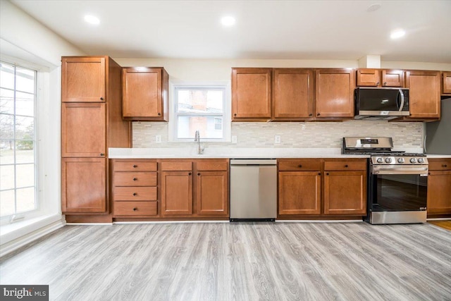 kitchen with brown cabinetry, stainless steel appliances, light wood finished floors, and light countertops
