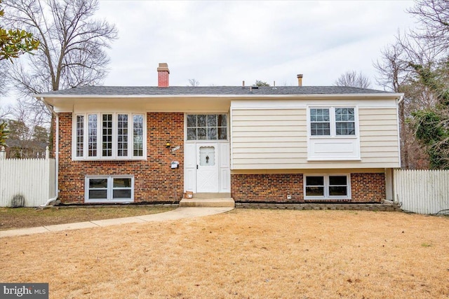 raised ranch featuring brick siding, a front yard, a chimney, and fence