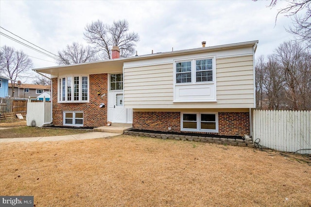 raised ranch with brick siding, a front lawn, and fence