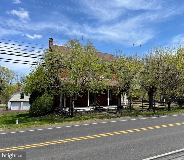 view of property hidden behind natural elements with fence, a chimney, and a porch