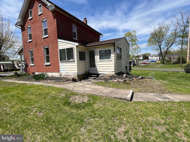 rear view of house featuring entry steps, a chimney, a lawn, and brick siding