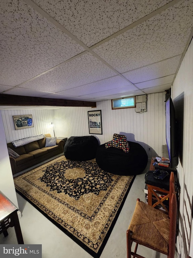 living area featuring wooden walls, concrete flooring, and a paneled ceiling