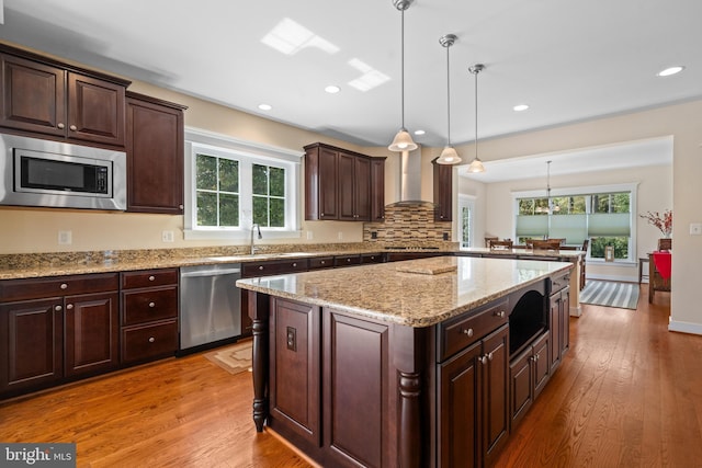kitchen with light wood-type flooring, wall chimney exhaust hood, appliances with stainless steel finishes, and a healthy amount of sunlight