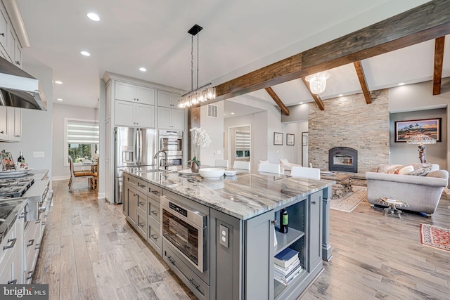 kitchen featuring gray cabinetry, open floor plan, light wood finished floors, and light stone counters