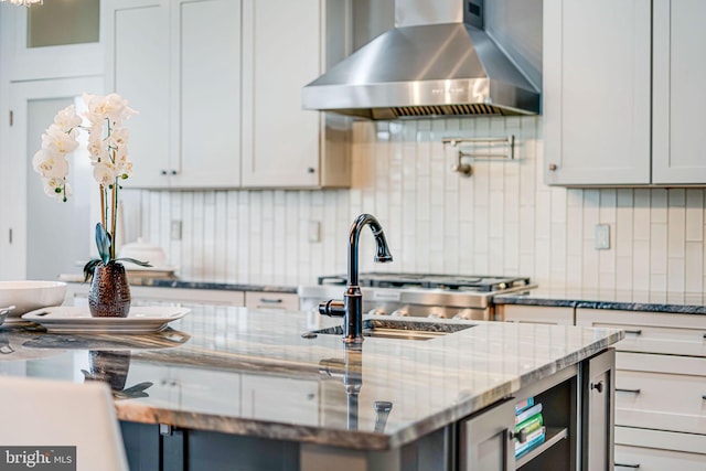kitchen with a sink, tasteful backsplash, light stone countertops, and wall chimney exhaust hood
