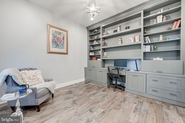office space with baseboards, light wood-type flooring, an inviting chandelier, and built in study area
