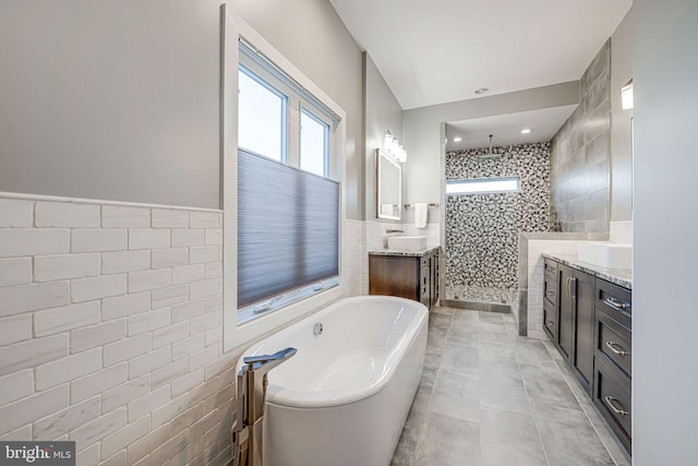 bathroom featuring a soaking tub, tile walls, vanity, wainscoting, and tiled shower