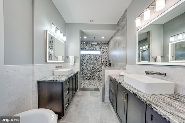 bathroom featuring tile walls, tiled shower, two vanities, and a sink