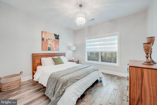 bedroom featuring hardwood / wood-style flooring, visible vents, a chandelier, and baseboards