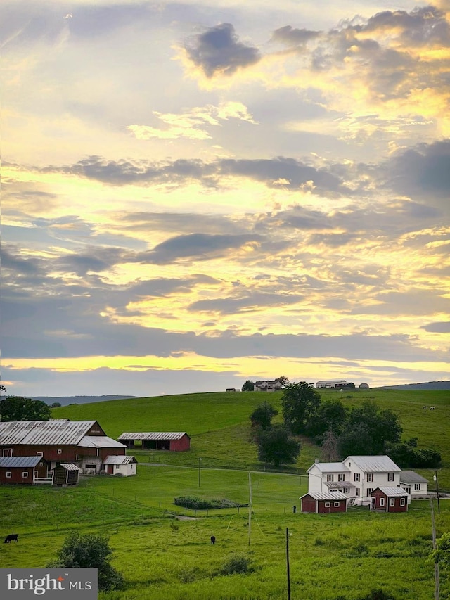 yard at dusk featuring fence, an outbuilding, and a rural view
