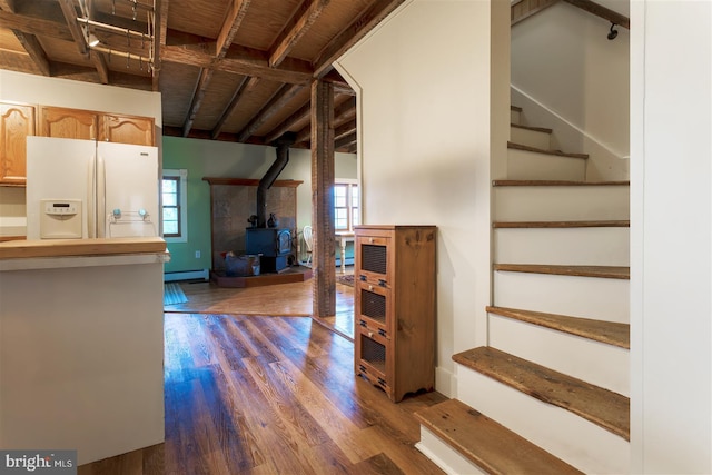 interior space featuring wood finished floors, a wood stove, a baseboard heating unit, baseboards, and white refrigerator with ice dispenser
