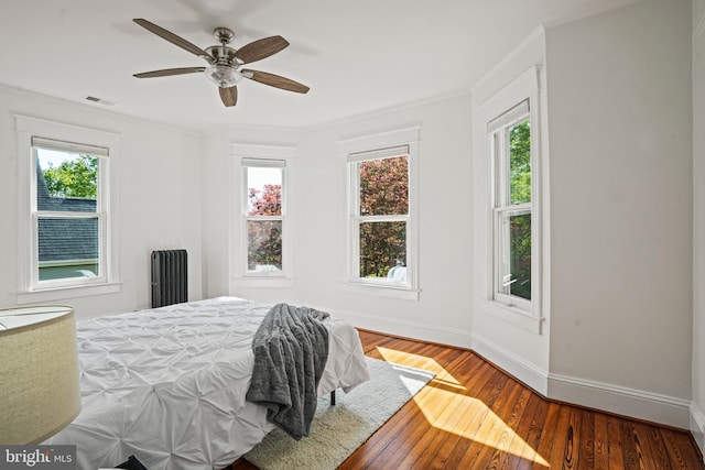 bedroom with ceiling fan, baseboards, visible vents, ornamental molding, and hardwood / wood-style flooring