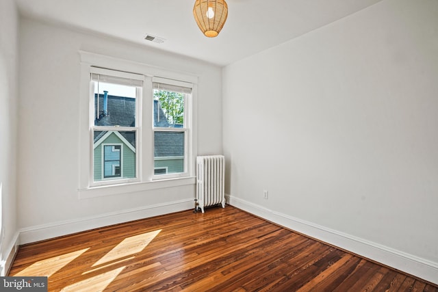 empty room featuring radiator, baseboards, hardwood / wood-style floors, and visible vents