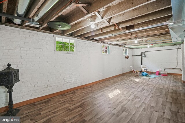 basement with baseboards, a wood stove, and wood finished floors