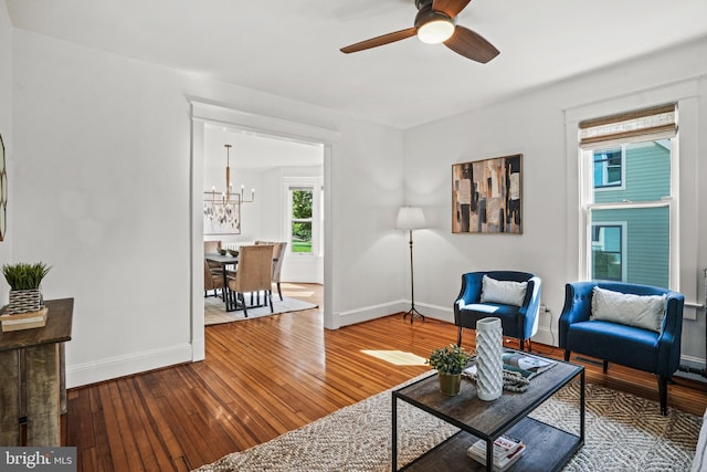 living area featuring wood-type flooring, baseboards, and ceiling fan with notable chandelier