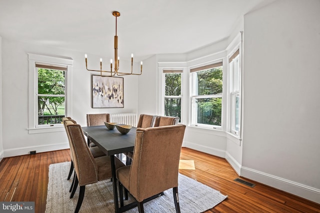 dining space featuring baseboards, visible vents, hardwood / wood-style floors, and a notable chandelier
