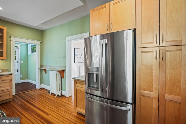 kitchen featuring dark wood-style flooring, glass insert cabinets, baseboards, radiator heating unit, and stainless steel fridge with ice dispenser