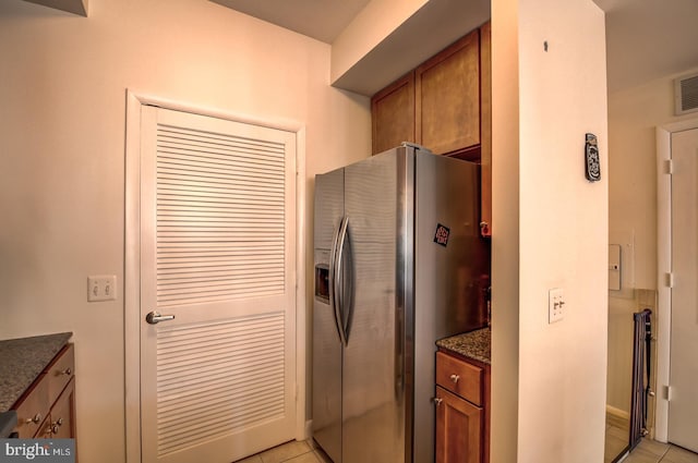kitchen featuring dark stone countertops, brown cabinets, light tile patterned floors, and stainless steel fridge with ice dispenser