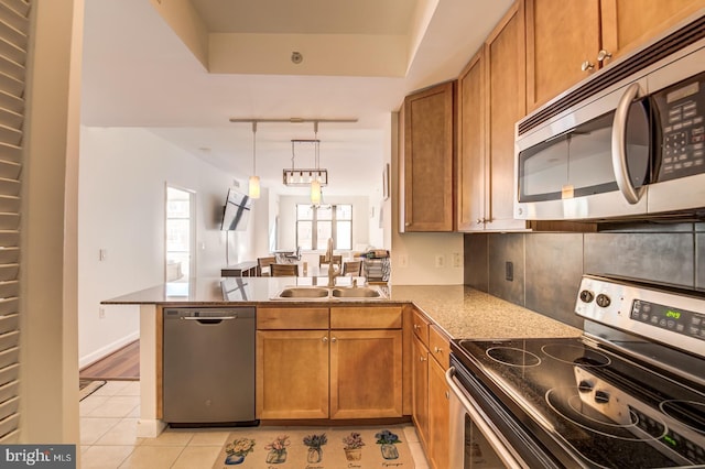 kitchen with a peninsula, a sink, appliances with stainless steel finishes, brown cabinets, and light tile patterned floors