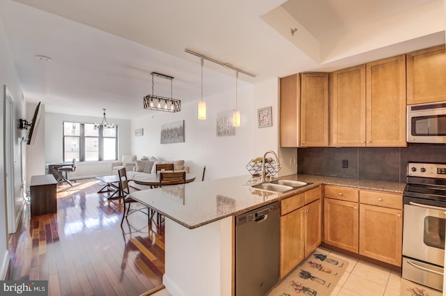 kitchen with a peninsula, a sink, light stone countertops, track lighting, and appliances with stainless steel finishes