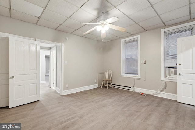 empty room with baseboard heating, a ceiling fan, wood finished floors, baseboards, and a paneled ceiling