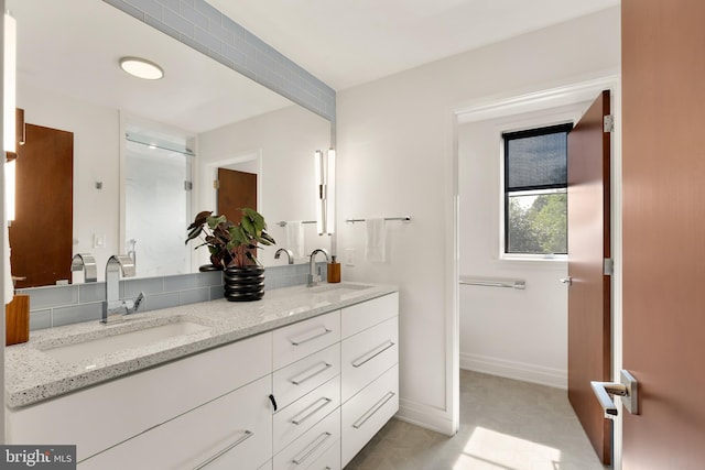 bathroom featuring a sink, baseboards, walk in shower, and double vanity