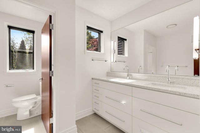 full bathroom with toilet, double vanity, baseboards, and a sink