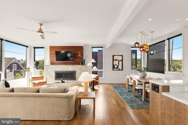 living area featuring ceiling fan, a fireplace, wood finished floors, baseboards, and beamed ceiling