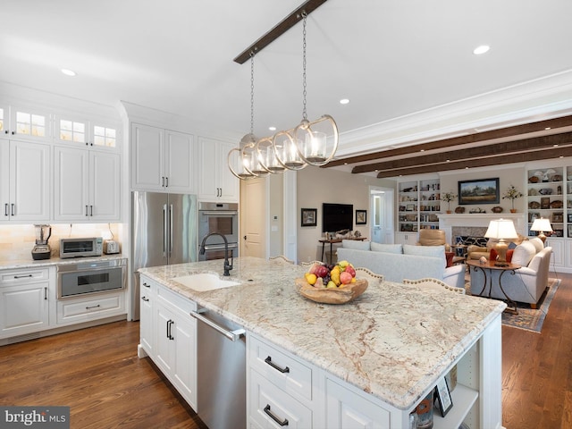 kitchen featuring white cabinets, dark wood-style flooring, appliances with stainless steel finishes, a sink, and an island with sink