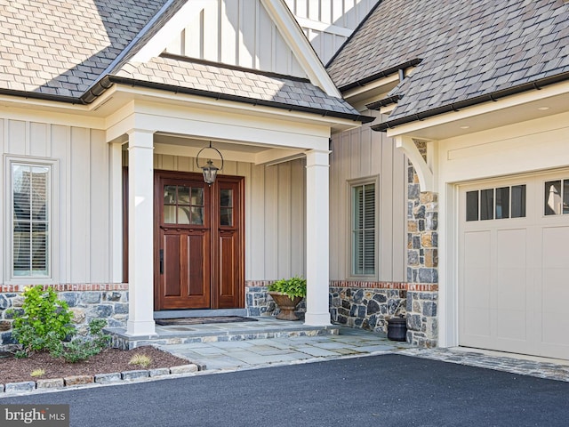 view of exterior entry with roof with shingles, board and batten siding, driveway, and stone siding