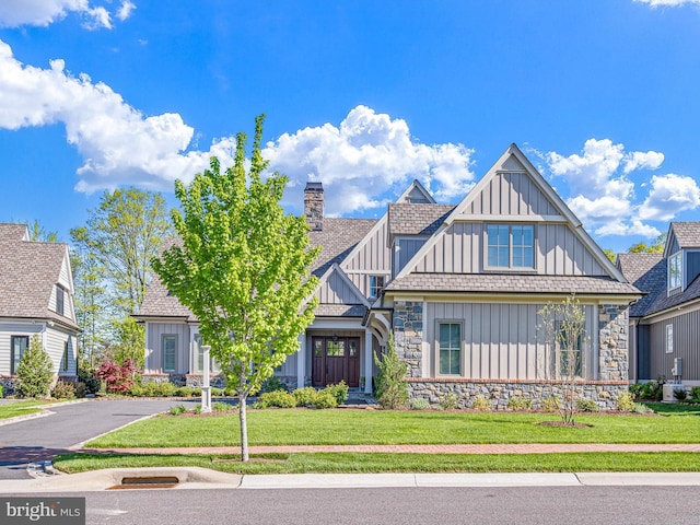 view of front facade featuring a chimney, a front lawn, board and batten siding, and stone siding