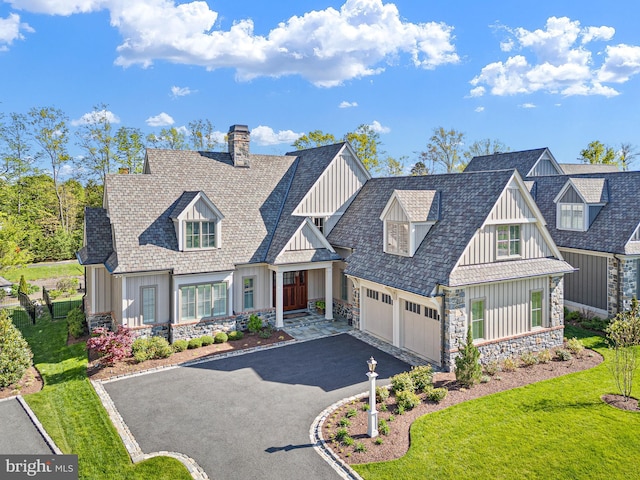 view of front of home featuring a front lawn, aphalt driveway, stone siding, a chimney, and board and batten siding