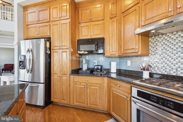 820 Belmont Bay Dr Unit 405, Woodbridge, VA 22191 - kitchen with under cabinet range hood, stainless steel appliances, backsplash, dark stone countertops, and wood finished floors