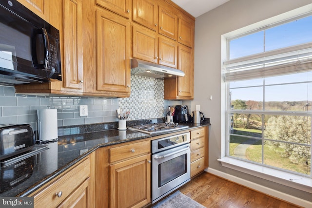 820 Belmont Bay Dr Unit 405, Woodbridge, VA 22191 - kitchen featuring light wood finished floors, under cabinet range hood, backsplash, dark stone counters, and appliances with stainless steel finishes